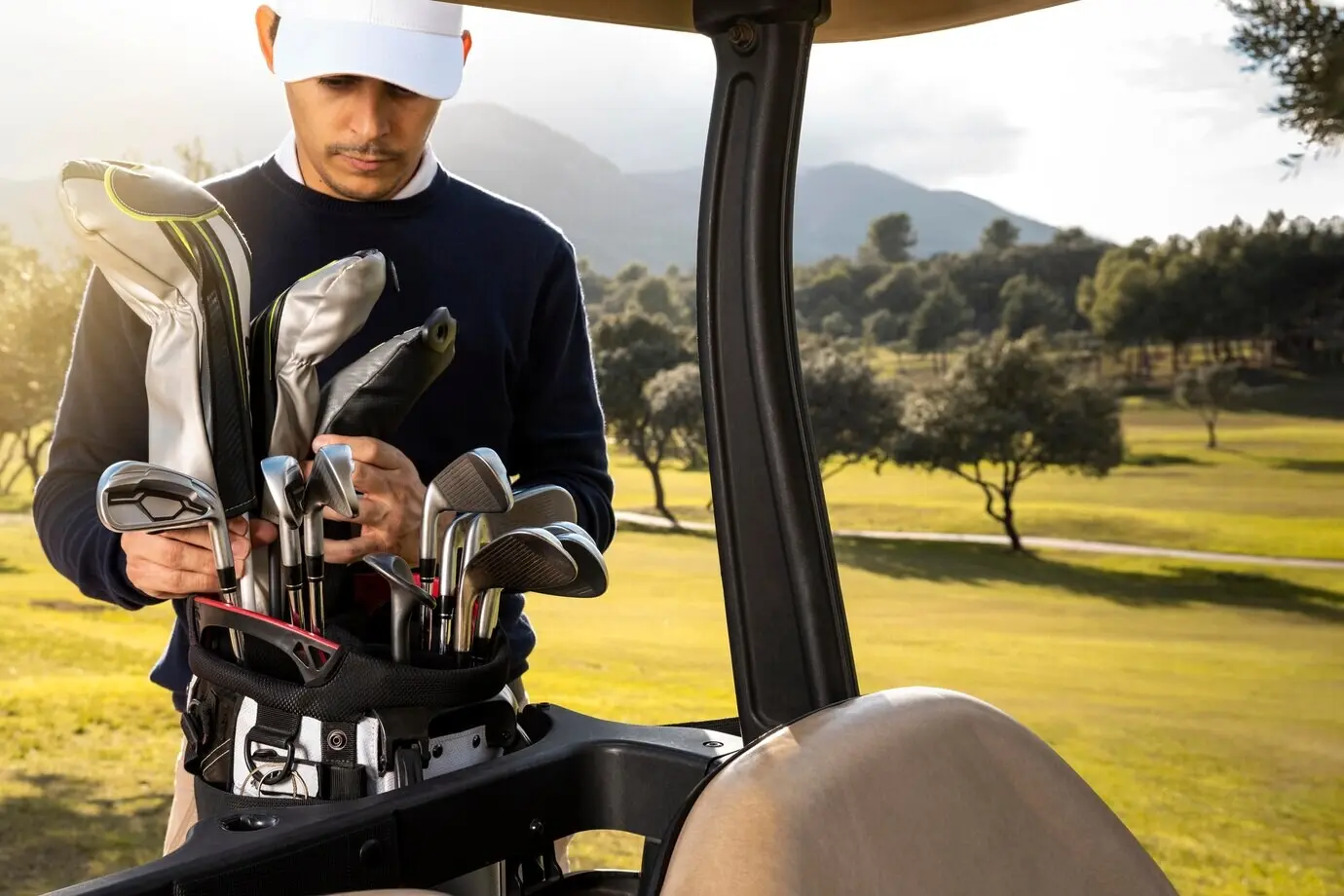 Front-facing view of a man placing clubs into a golf cart.
