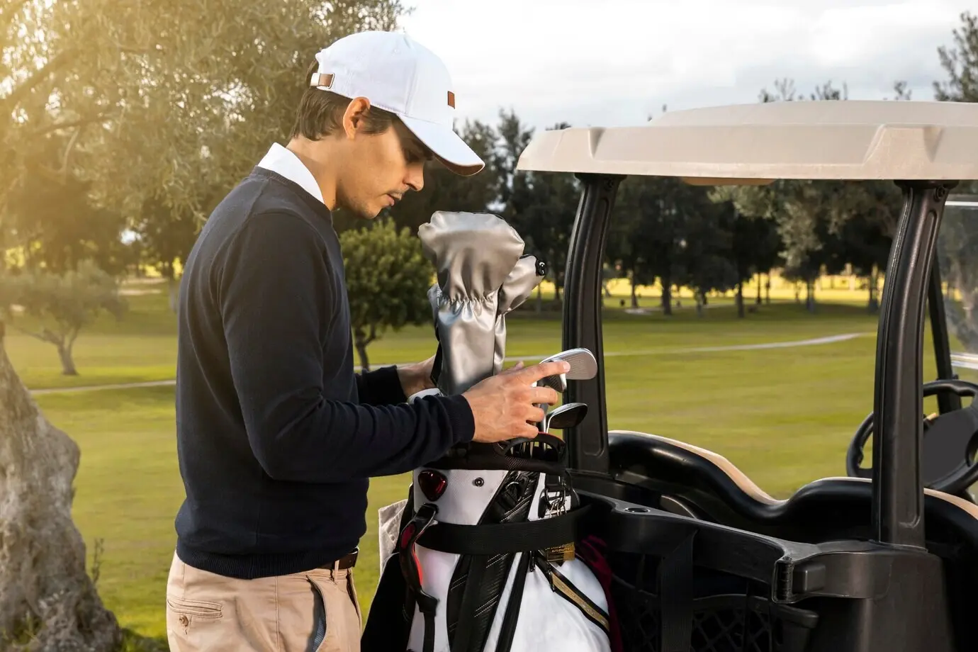 Side view of a man placing clubs into a golf cart